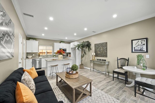 living room with light wood-type flooring, crown molding, and sink