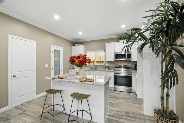 kitchen with appliances with stainless steel finishes, a kitchen island, white cabinetry, sink, and light stone counters