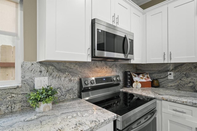 kitchen with light stone countertops, decorative backsplash, appliances with stainless steel finishes, and white cabinetry