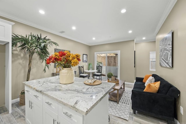 kitchen featuring white cabinets, light stone counters, ornamental molding, and a kitchen island