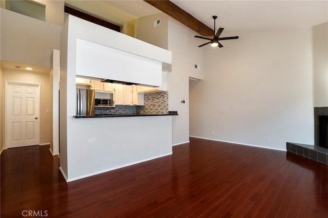 unfurnished living room featuring ceiling fan, beamed ceiling, high vaulted ceiling, dark hardwood / wood-style floors, and a tiled fireplace