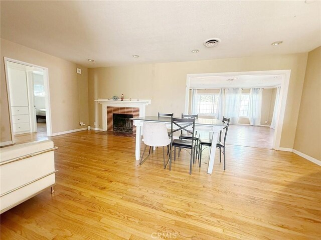 dining space with a brick fireplace and light hardwood / wood-style flooring