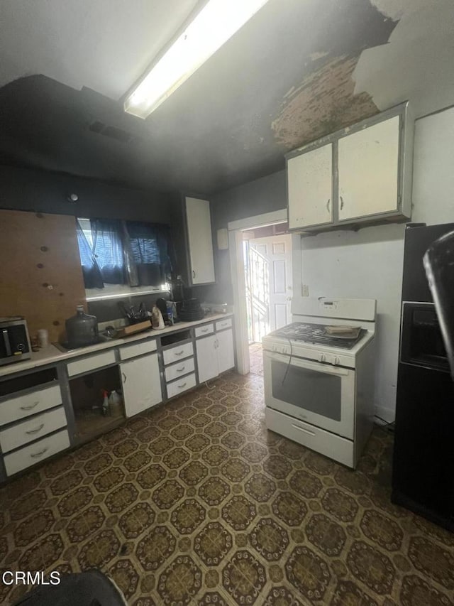 kitchen featuring white cabinets, black refrigerator, and white gas stove