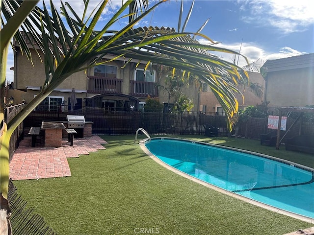 view of pool with a lawn, exterior kitchen, and a patio