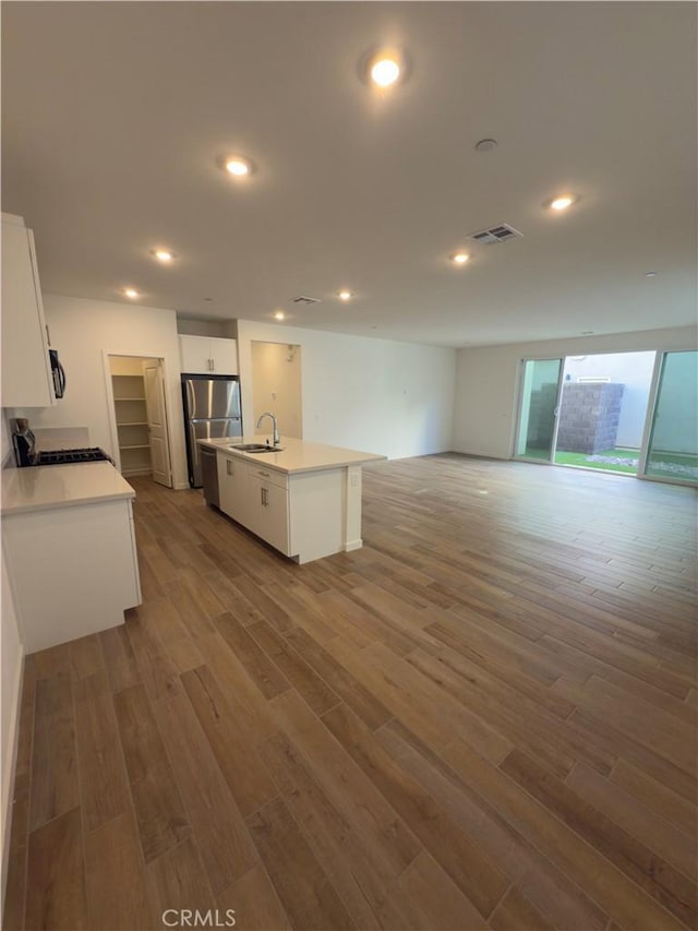 kitchen with sink, hardwood / wood-style flooring, a kitchen island with sink, white cabinets, and stainless steel fridge