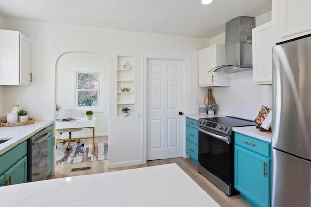 kitchen with wall chimney range hood, appliances with stainless steel finishes, backsplash, white cabinets, and blue cabinets