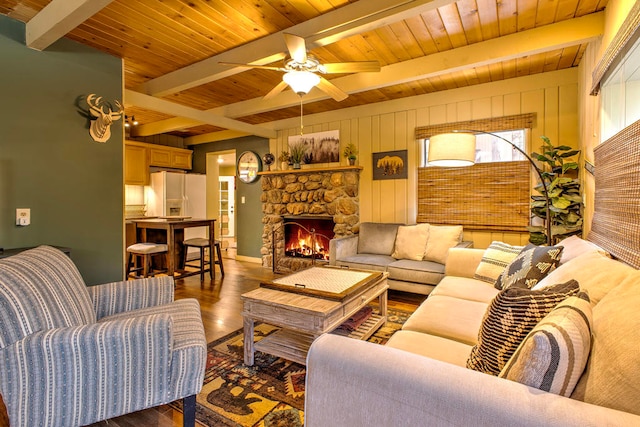 living room featuring wood walls, a stone fireplace, ceiling fan, wood-type flooring, and beamed ceiling