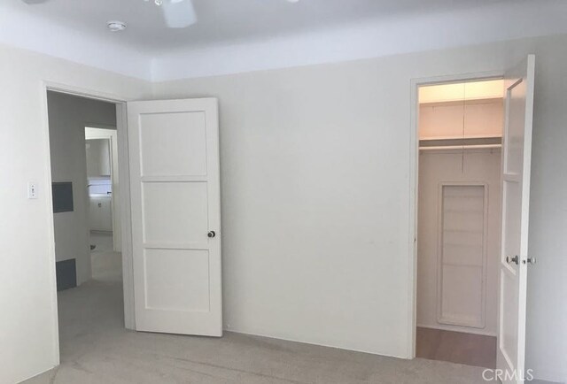 unfurnished bedroom featuring ceiling fan, light carpet, a closet, and a walk in closet