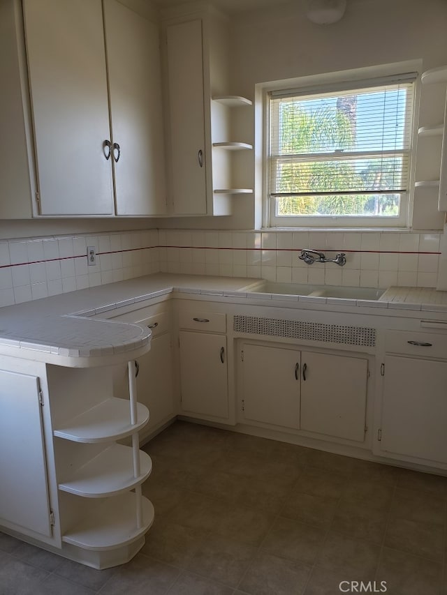 kitchen featuring white cabinetry, tile countertops, backsplash, and sink