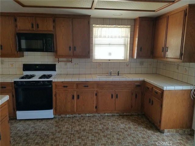 kitchen featuring decorative backsplash, sink, black appliances, and tile counters