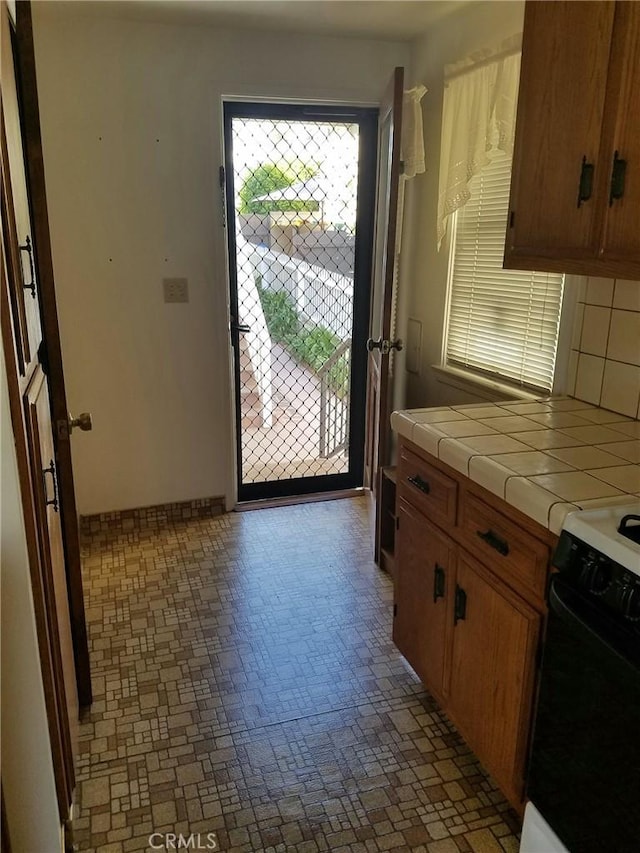 kitchen with decorative backsplash, black range with electric stovetop, and tile counters