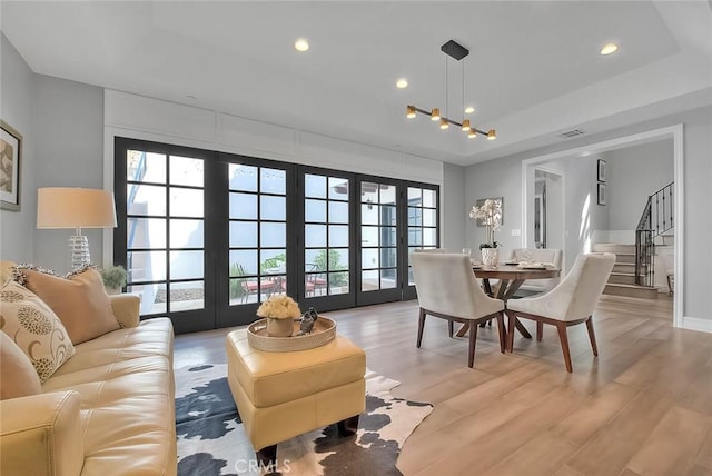 living room featuring a tray ceiling, french doors, and light wood-type flooring