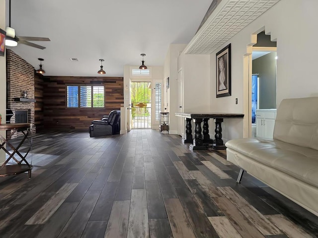 living area with a brick fireplace, dark hardwood / wood-style flooring, wood walls, and ceiling fan