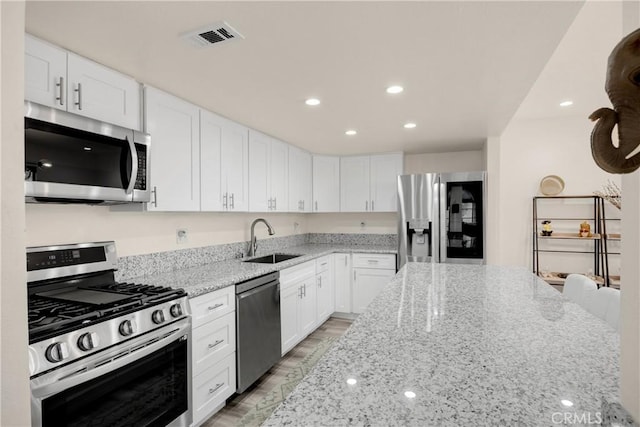 kitchen featuring white cabinets, a kitchen bar, stainless steel appliances, sink, and light stone counters