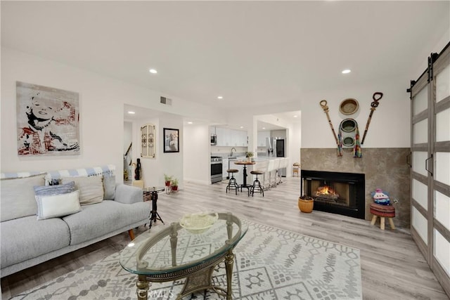 living room featuring sink, light hardwood / wood-style flooring, a barn door, and a fireplace