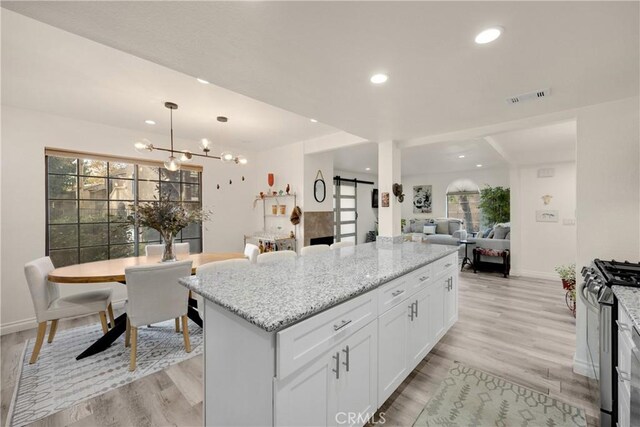 kitchen featuring a barn door, pendant lighting, stainless steel range with gas stovetop, white cabinetry, and light stone countertops