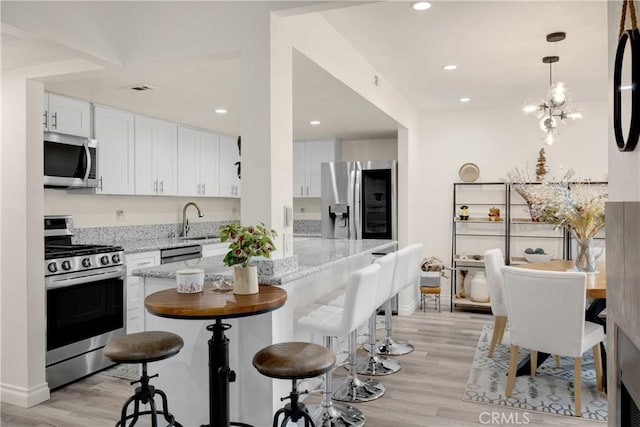 kitchen featuring hanging light fixtures, light wood-type flooring, appliances with stainless steel finishes, white cabinets, and light stone counters