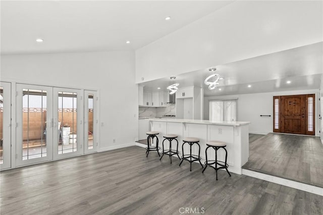 kitchen with kitchen peninsula, a breakfast bar, dark wood-type flooring, white cabinets, and backsplash