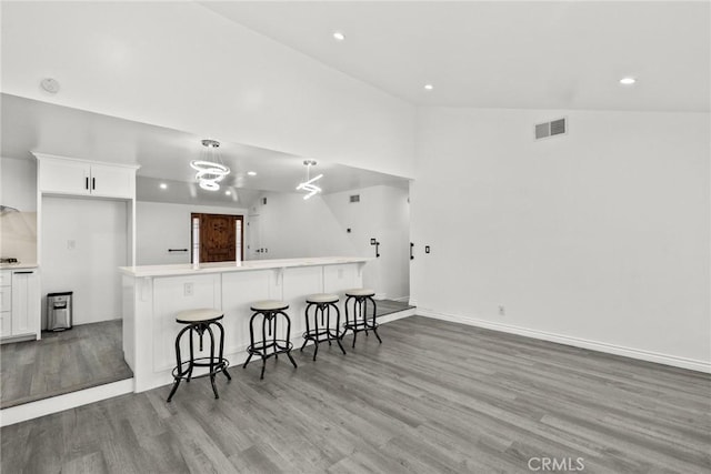 kitchen with a breakfast bar area, white cabinetry, light hardwood / wood-style floors, and vaulted ceiling