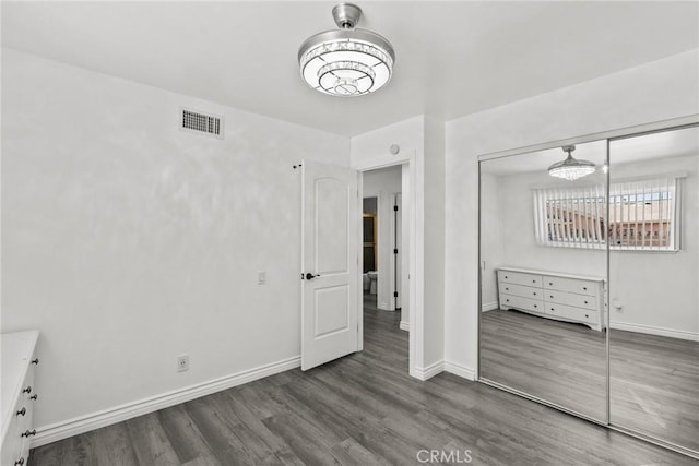 unfurnished bedroom with dark wood-type flooring, an inviting chandelier, and a closet