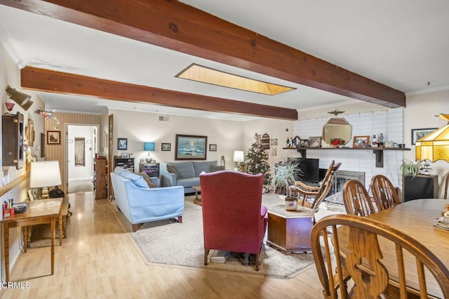 living room featuring a brick fireplace, ornamental molding, beam ceiling, and light hardwood / wood-style flooring