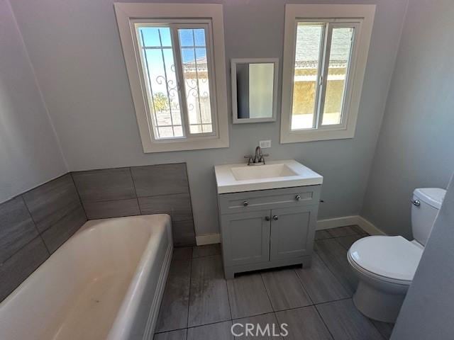 full bathroom with toilet, a garden tub, baseboards, and vanity