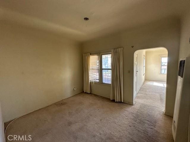 empty room with arched walkways, light colored carpet, and plenty of natural light