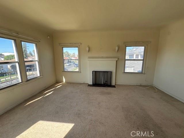 unfurnished living room with plenty of natural light, a fireplace with flush hearth, and light colored carpet