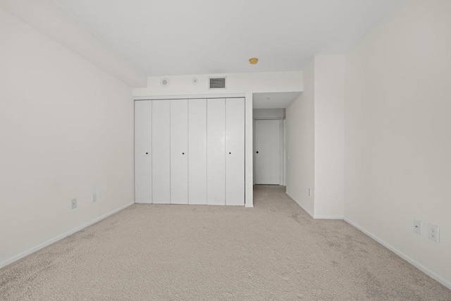 unfurnished bedroom with light colored carpet and a closet