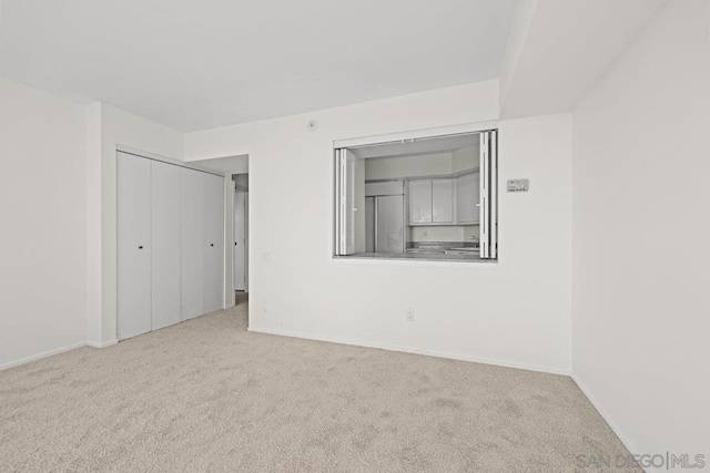 unfurnished bedroom featuring light colored carpet, a closet, and stainless steel built in refrigerator