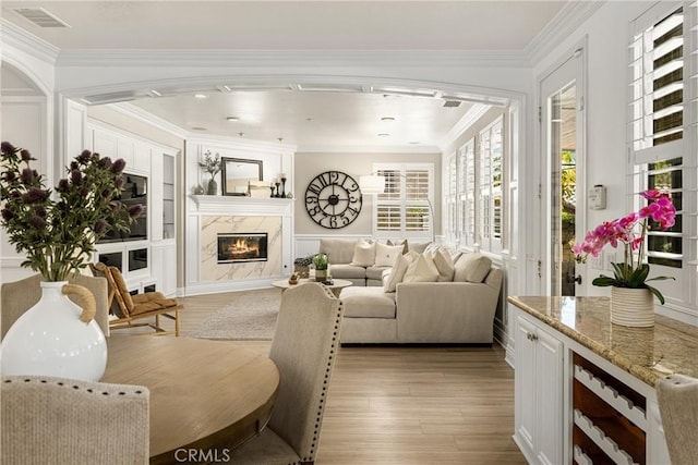 living room with a premium fireplace, crown molding, beverage cooler, and light hardwood / wood-style flooring