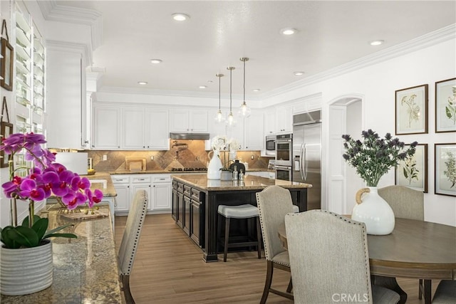 kitchen with appliances with stainless steel finishes, light stone counters, white cabinetry, and a kitchen island