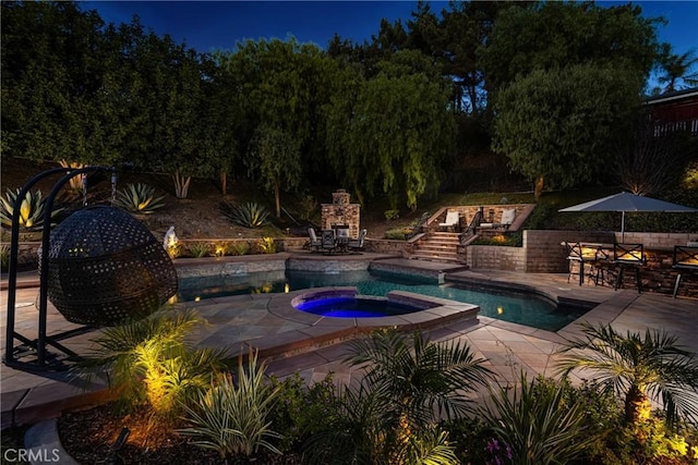 view of swimming pool with an outdoor stone fireplace, an in ground hot tub, and a patio