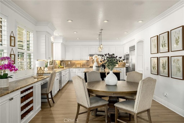 dining area featuring sink, wood-type flooring, and crown molding