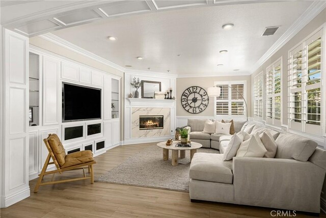 living room featuring a premium fireplace, ornamental molding, wood-type flooring, and built in shelves