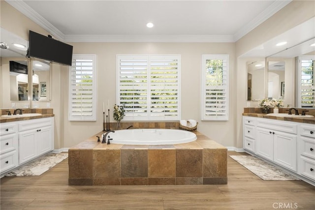 bathroom with crown molding, a relaxing tiled tub, and vanity