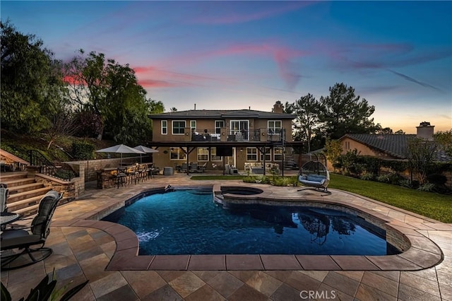 pool at dusk featuring a patio area, an in ground hot tub, and a bar