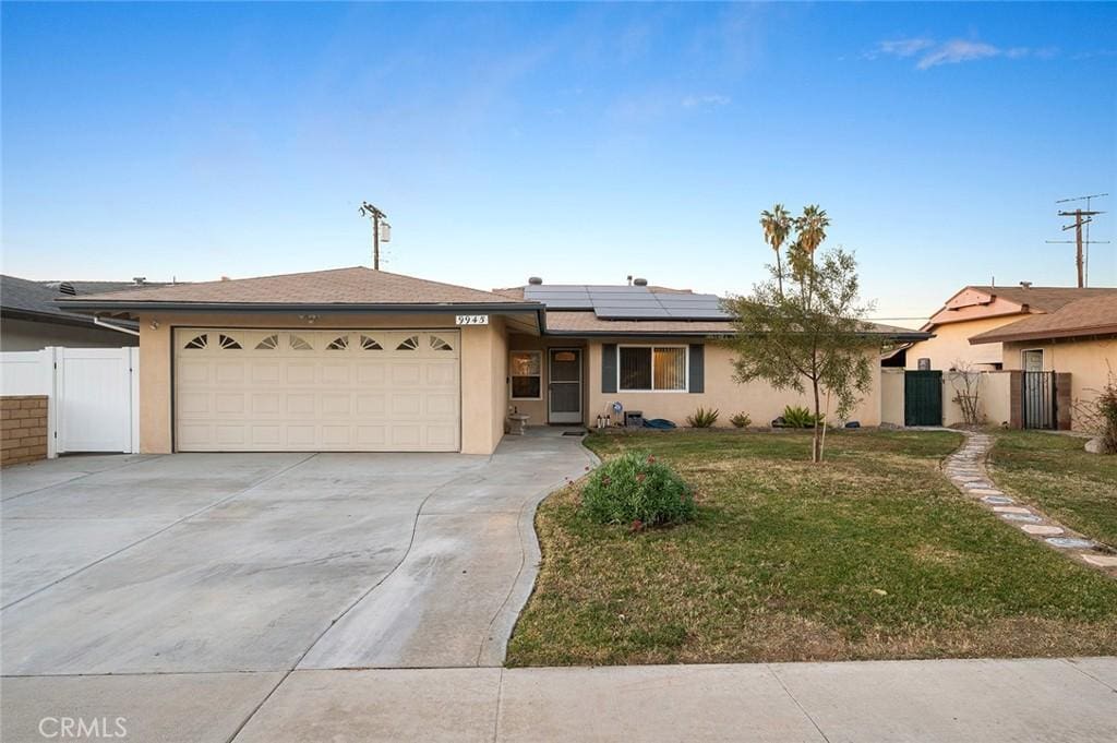 ranch-style home with a front yard, a garage, and solar panels