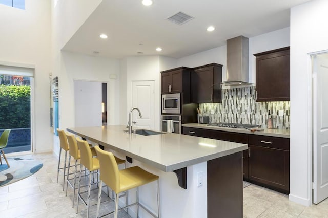 kitchen featuring tasteful backsplash, sink, a kitchen island with sink, stainless steel appliances, and wall chimney exhaust hood