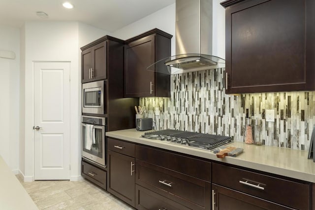 kitchen with backsplash, appliances with stainless steel finishes, wall chimney range hood, and dark brown cabinets