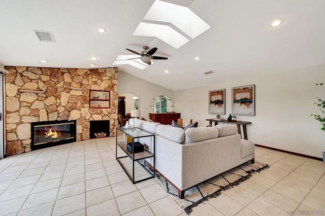 living room with ceiling fan, light tile patterned floors, lofted ceiling with skylight, and a stone fireplace