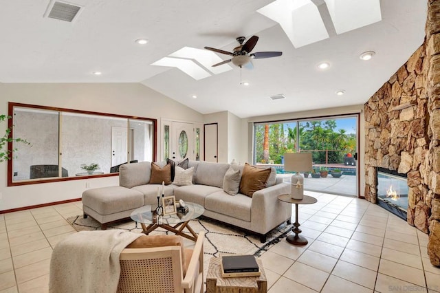 living room featuring ceiling fan, light tile patterned flooring, a fireplace, and lofted ceiling with skylight