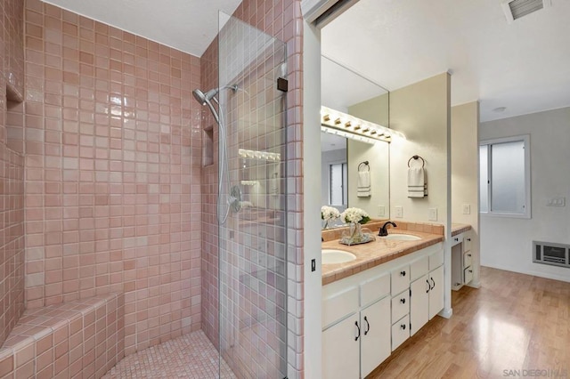 bathroom with wood-type flooring, tiled shower, and vanity