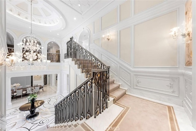 stairway featuring a towering ceiling, crown molding, and a notable chandelier