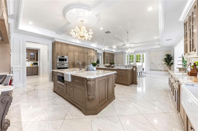 kitchen featuring light stone countertops, ornamental molding, a raised ceiling, and a kitchen island with sink