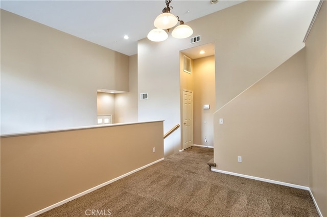 carpeted empty room with a towering ceiling and a chandelier