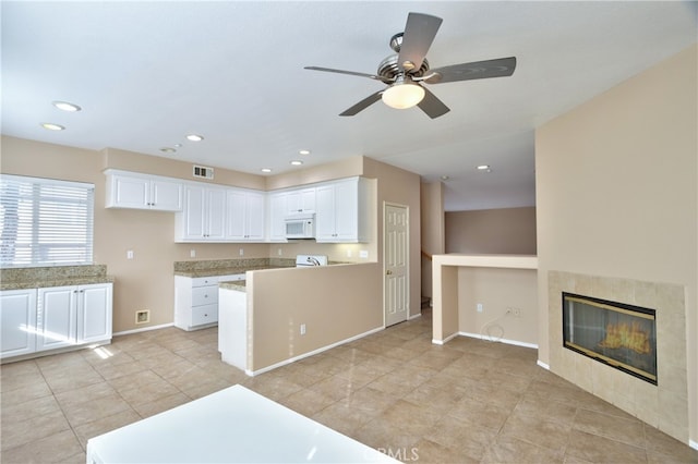 kitchen featuring ceiling fan, light tile patterned floors, a tile fireplace, and white cabinetry