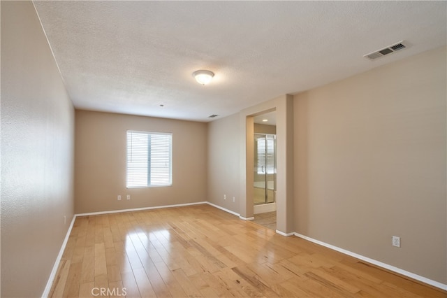 empty room with a textured ceiling and light hardwood / wood-style flooring