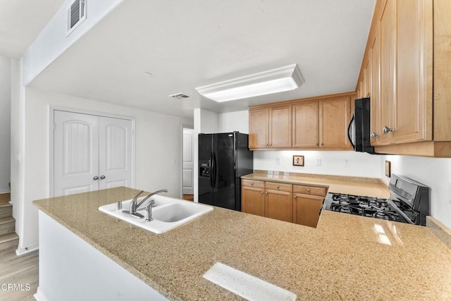 kitchen with kitchen peninsula, light stone countertops, black appliances, and sink