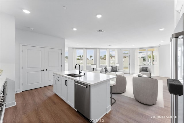 kitchen featuring sink, white cabinets, stainless steel dishwasher, light hardwood / wood-style floors, and a center island with sink